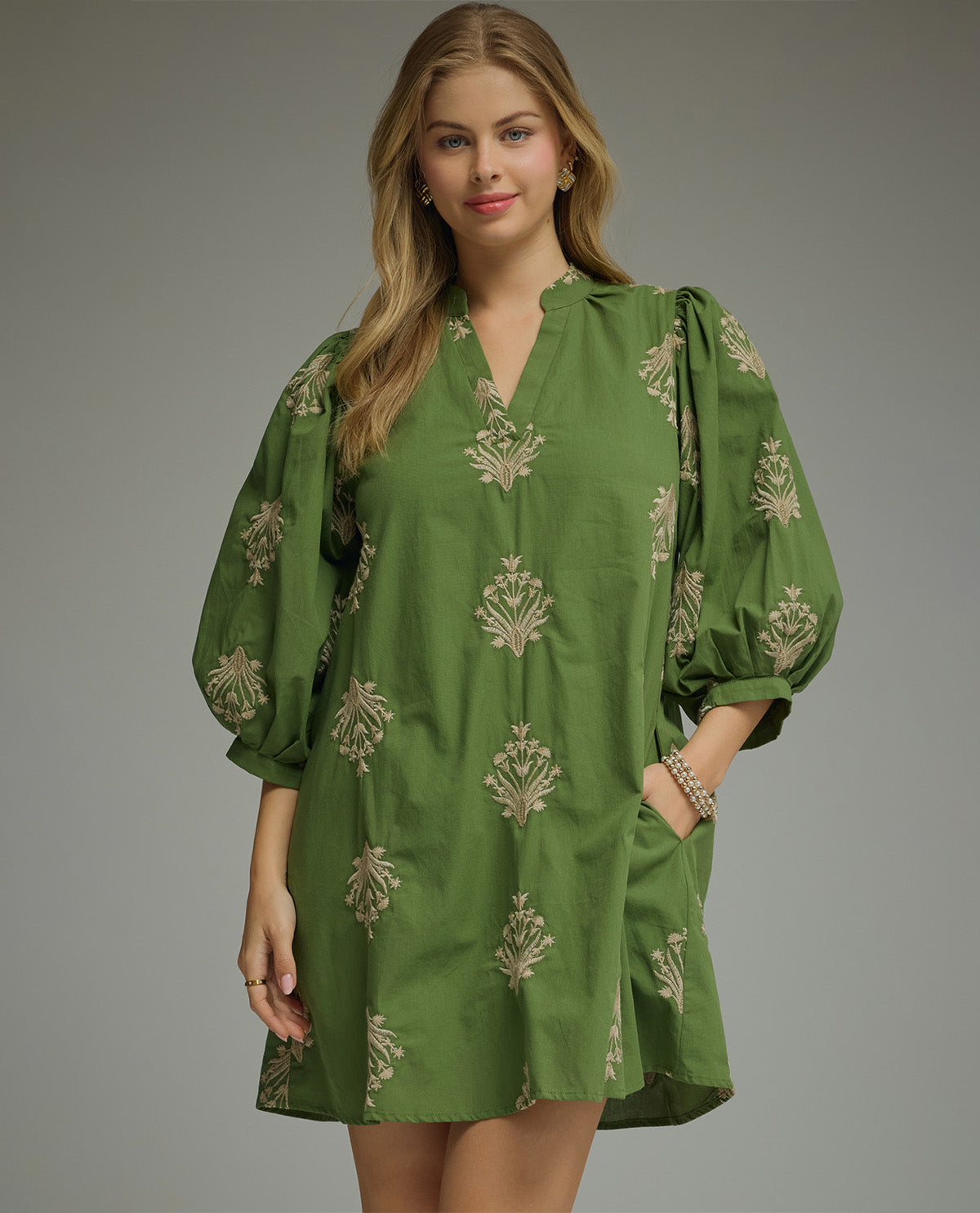 Woman wearing a green dress with floral patterns on a gray background