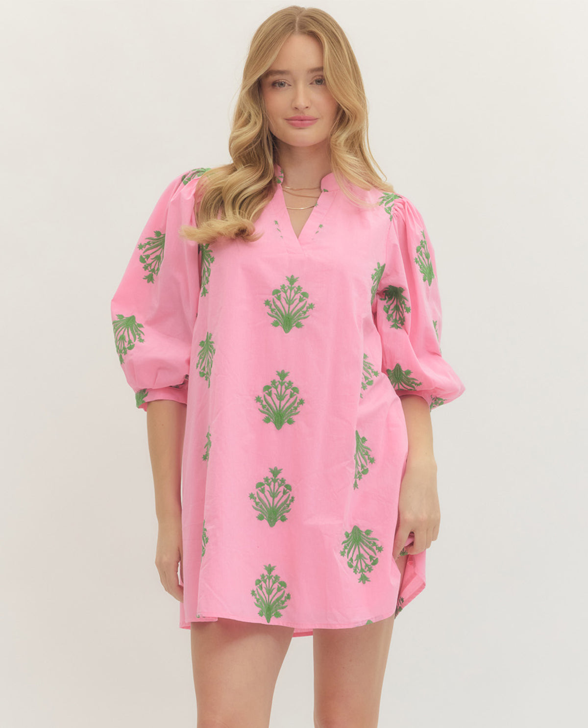 Woman wearing a pink dress with green patterns on a white background
