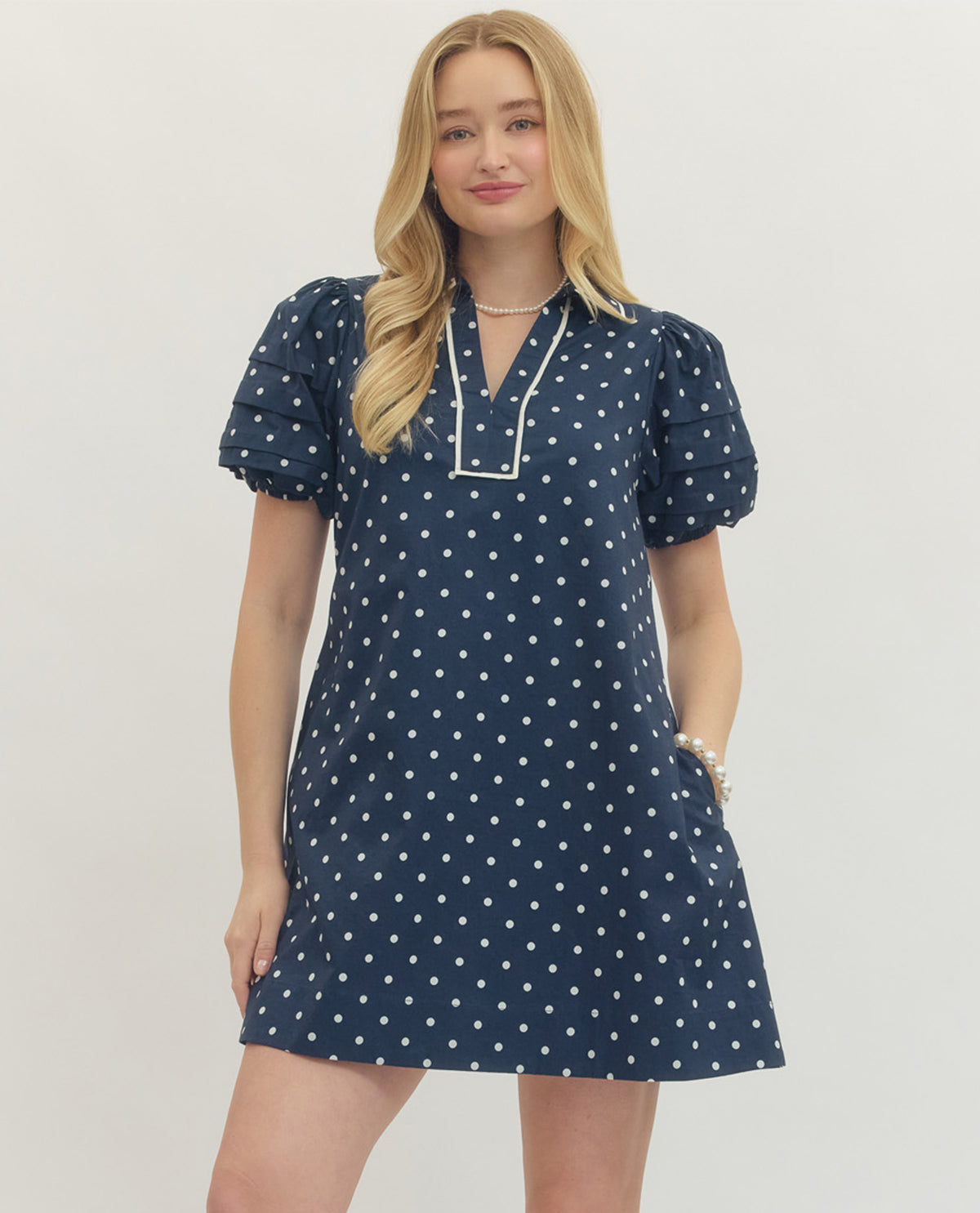 Woman wearing a navy dress with white polka dots on a plain background
