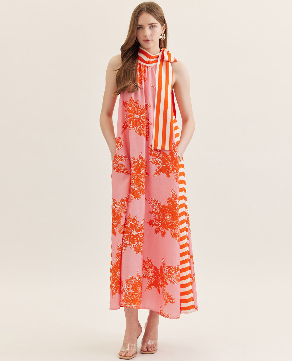 Woman wearing a sleeveless dress with orange floral and white striped pattern on a plain background