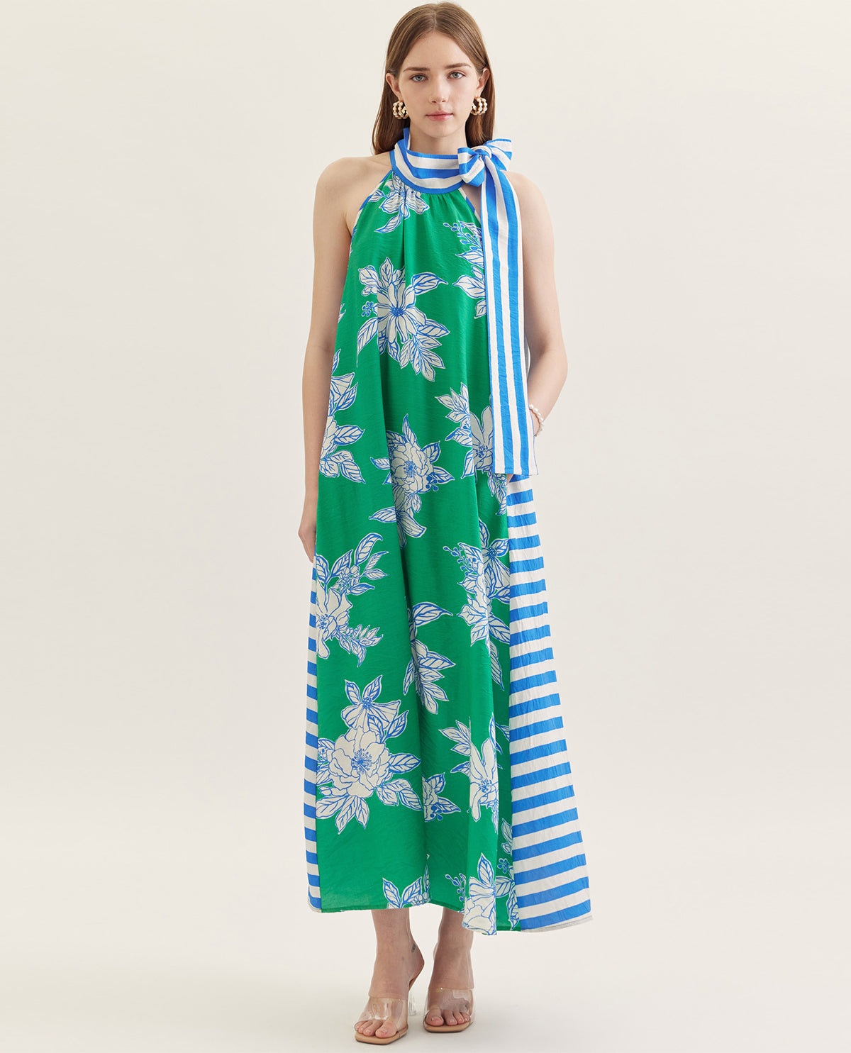 Woman wearing a green floral dress with a blue and white striped scarf on a white background