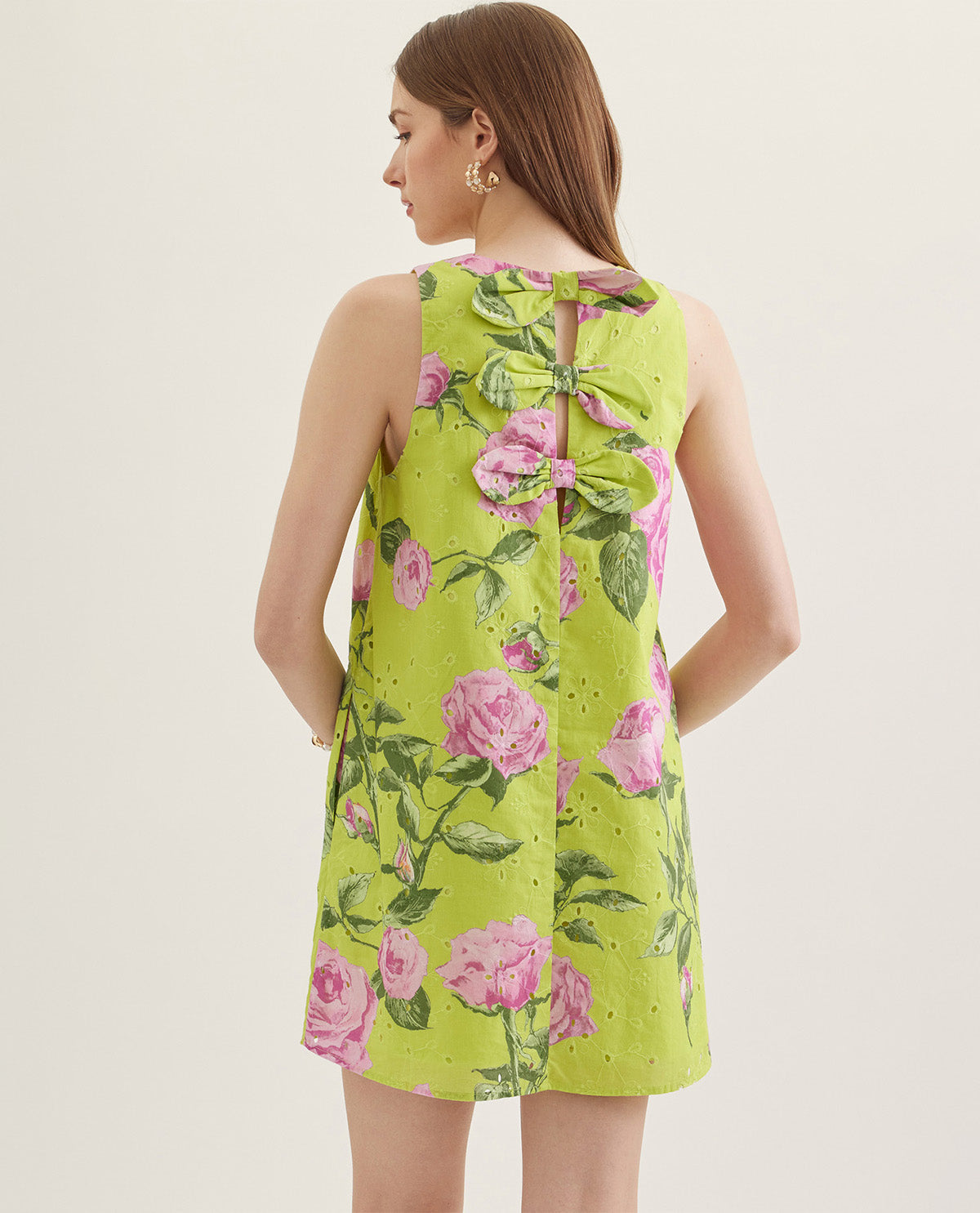 Woman wearing a green floral dress with pink roses on a plain background