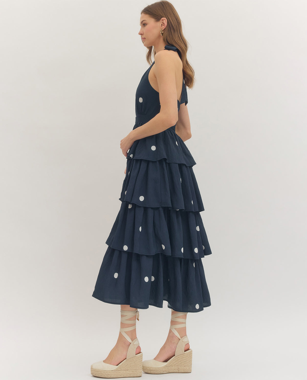 Woman wearing a navy tiered dress with white polka dots on a plain background