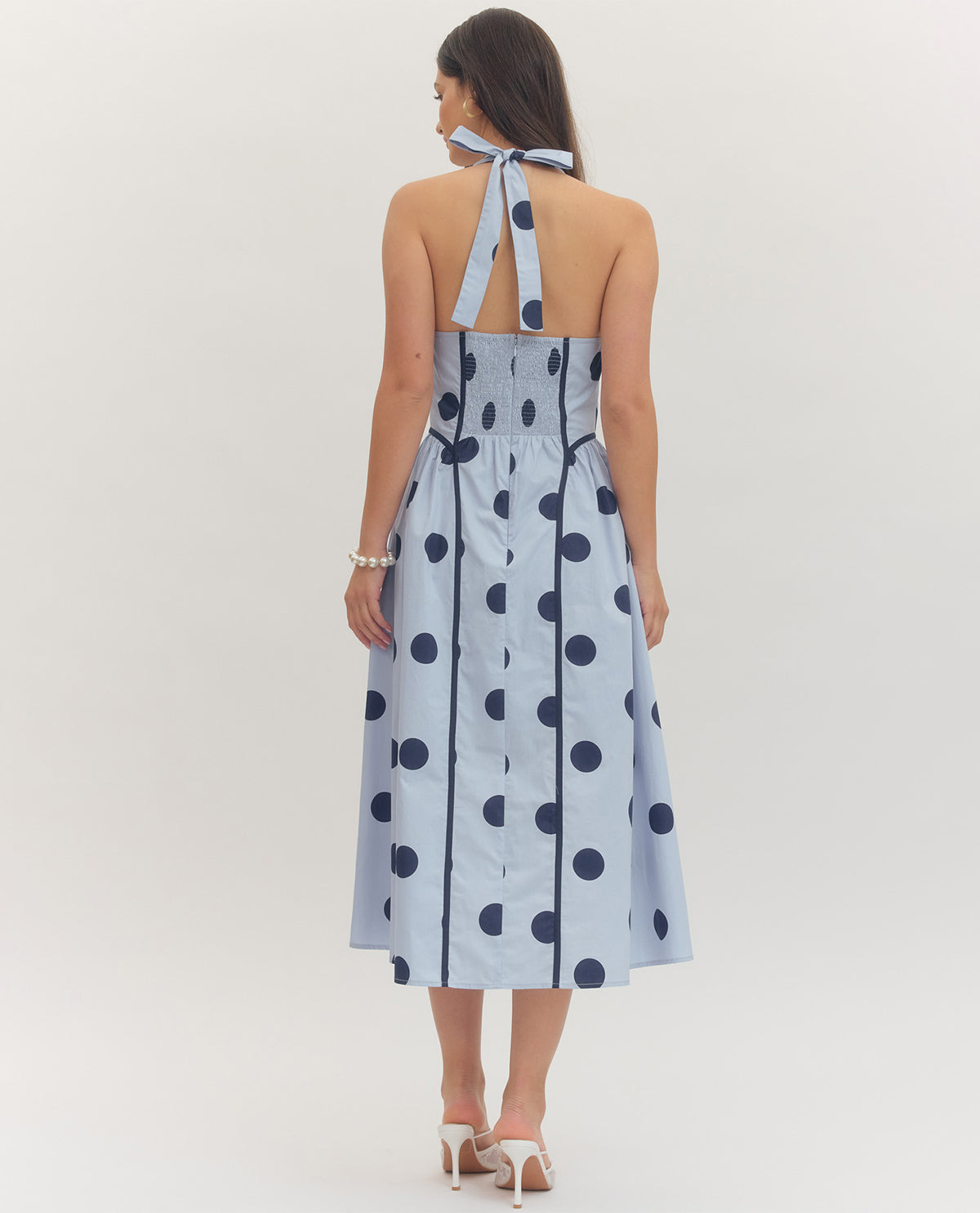 Woman wearing a light blue dress with dark blue polka dots on a white background