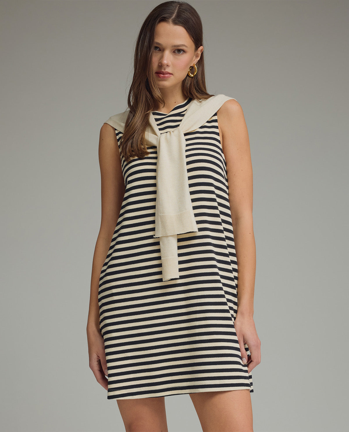 Woman wearing a black and white striped dress with a beige scarf on a gray background