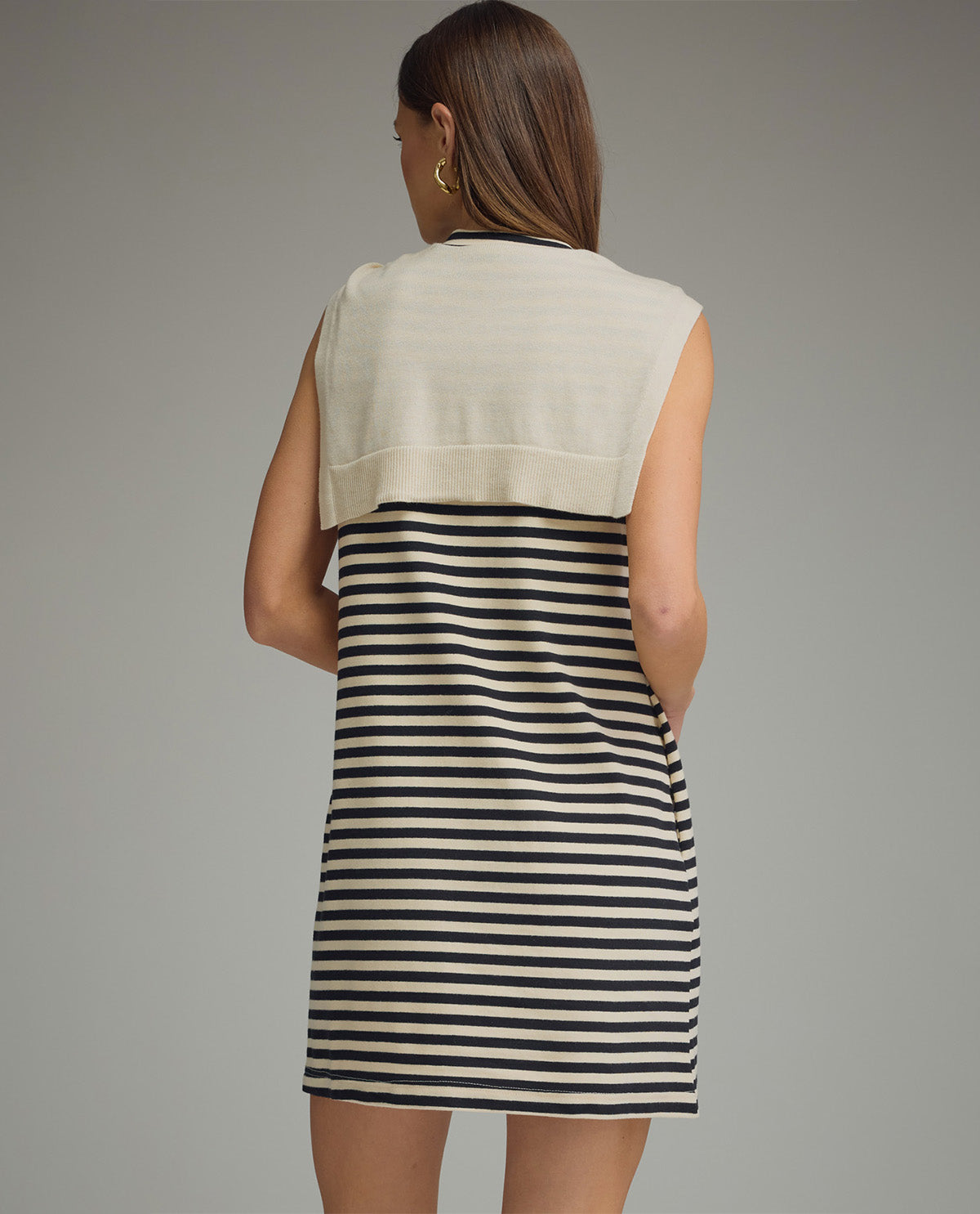 Woman wearing a sleeveless dress with beige top and black and white striped skirt on a gray background
