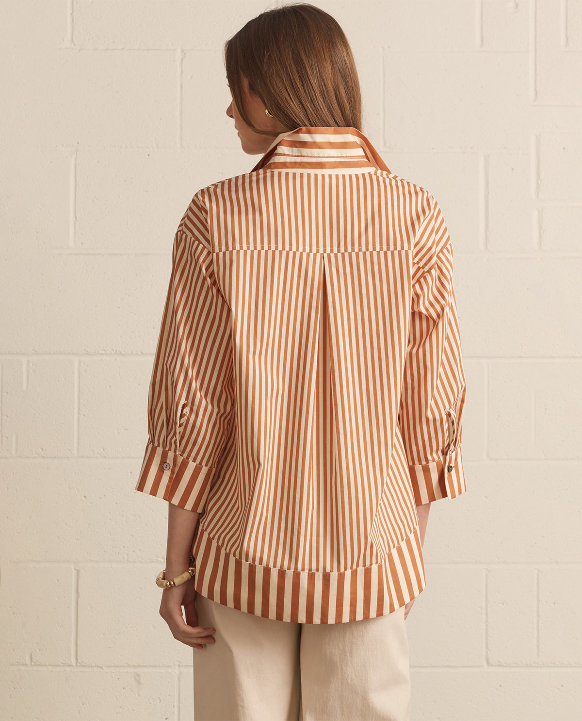 Woman wearing a striped shirt against a white brick wall