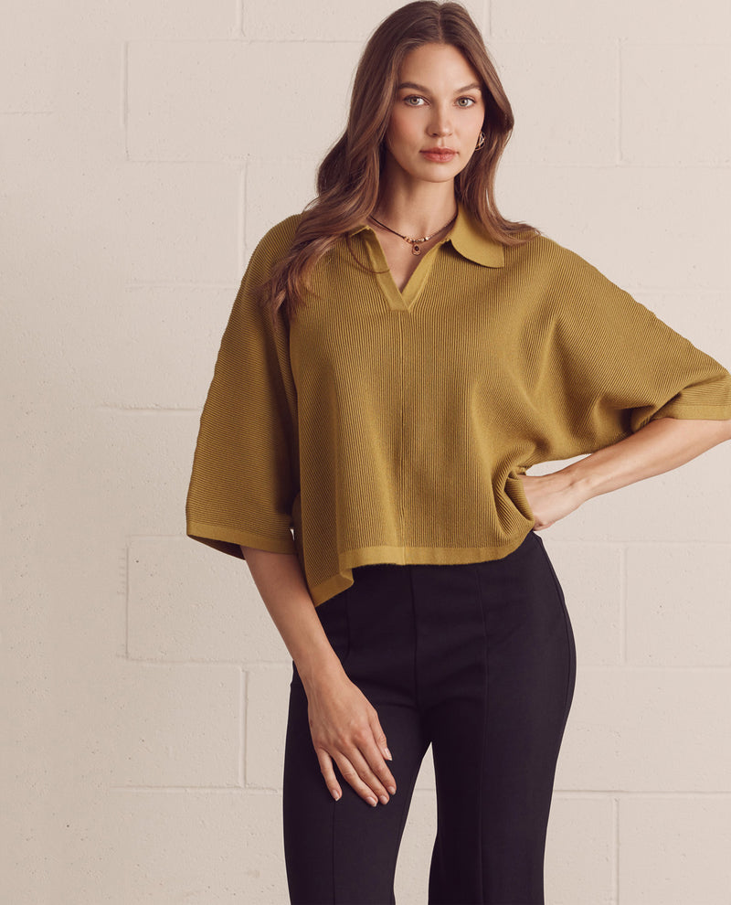 Woman wearing a mustard yellow blouse and black pants against a light background