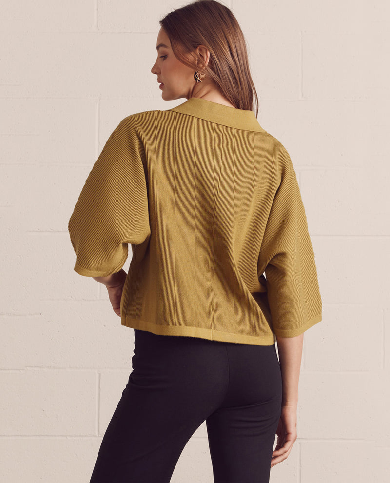 Woman wearing a mustard yellow blouse against a white wall