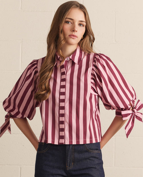 Woman wearing a striped blouse with tied sleeves against a white wall