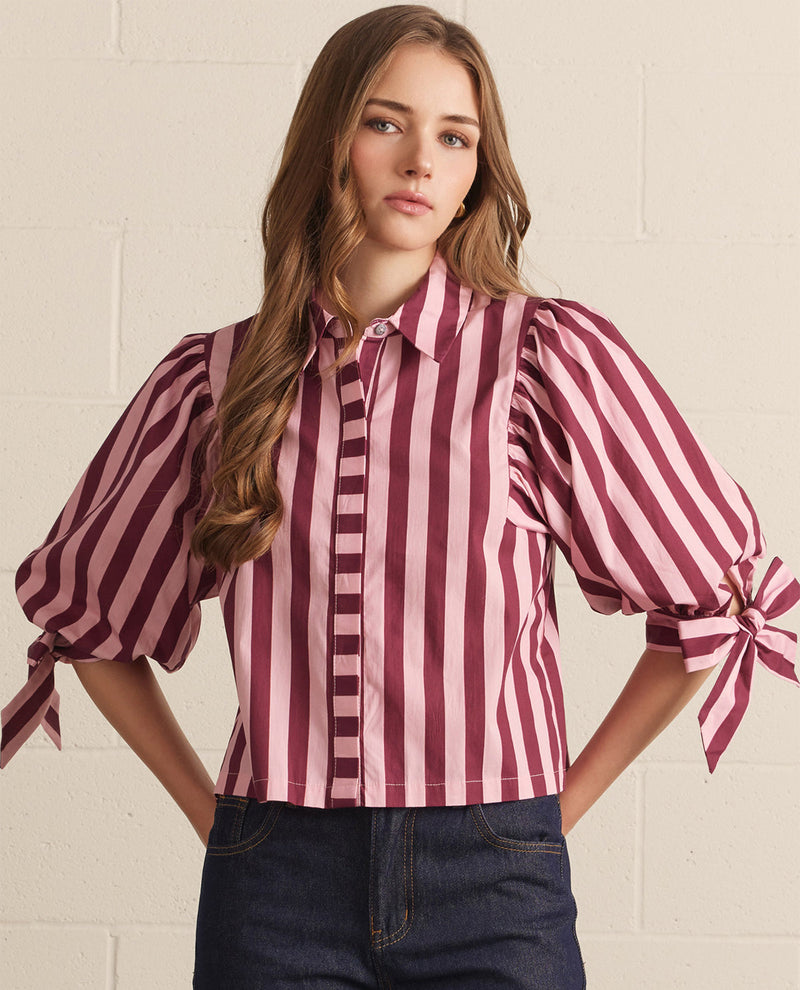 Woman wearing a striped blouse with tied sleeves against a white wall