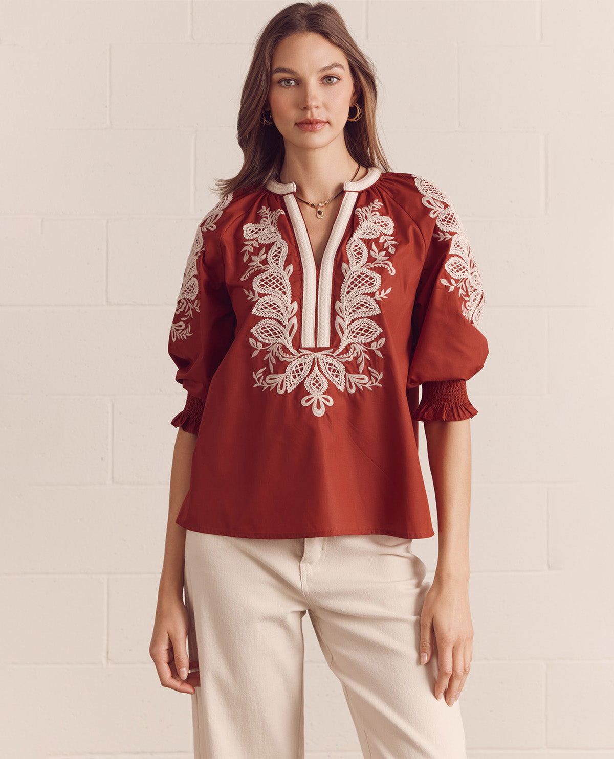 Woman wearing a red blouse with white lace details on a beige background