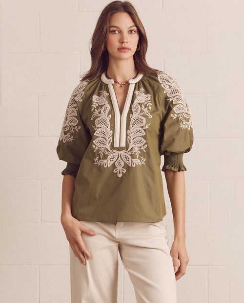 Woman wearing a green blouse with white embroidery against a light background