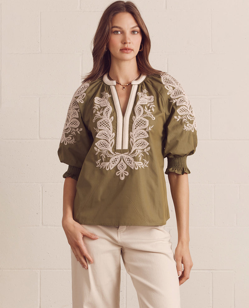 Woman wearing a green blouse with white embroidery against a light background