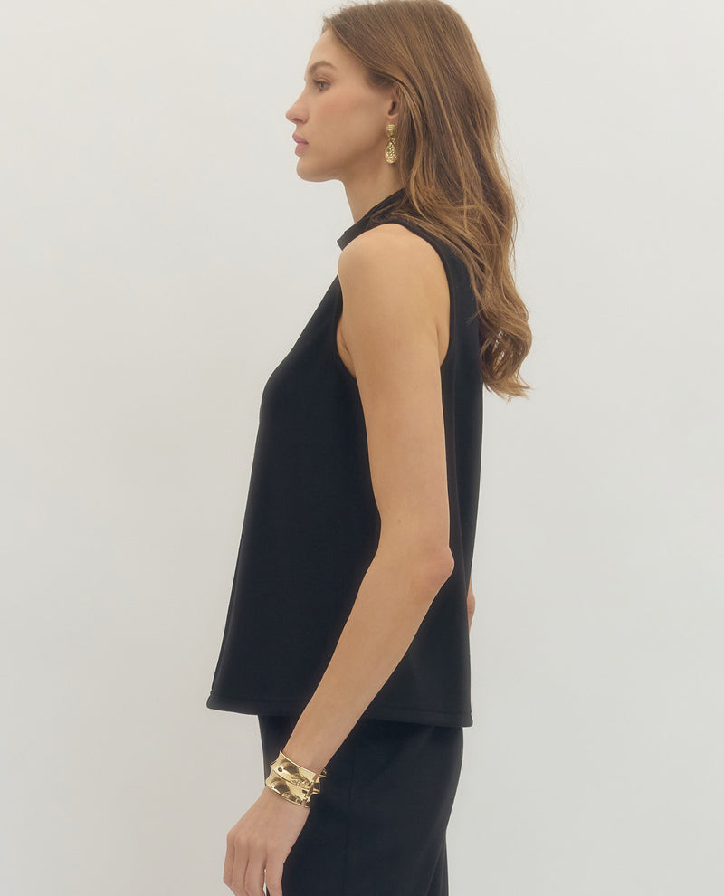 Woman wearing a black sleeveless top and black pants against a white background
