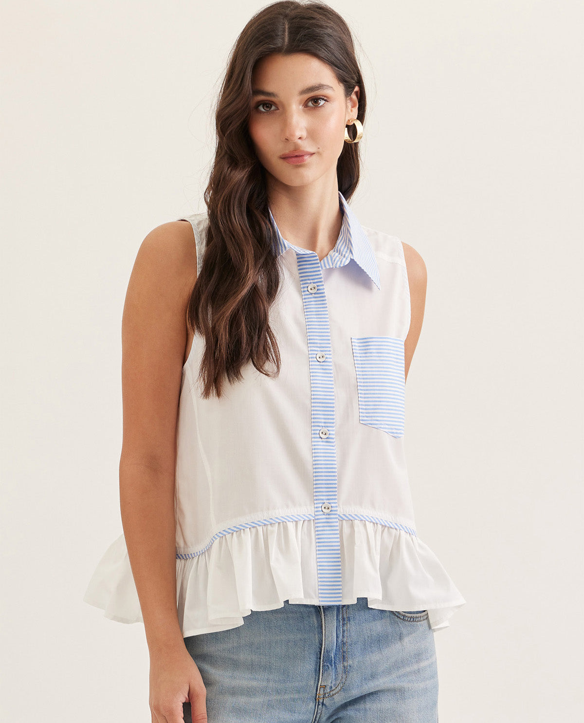 Woman wearing a sleeveless white blouse with blue striped trim against a plain background