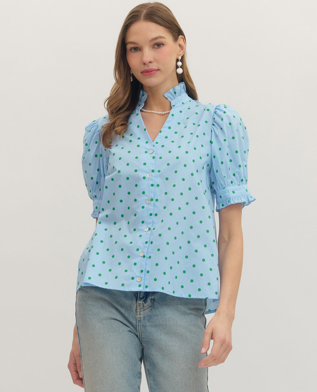 Woman wearing a light blue blouse with green polka dots on a plain background