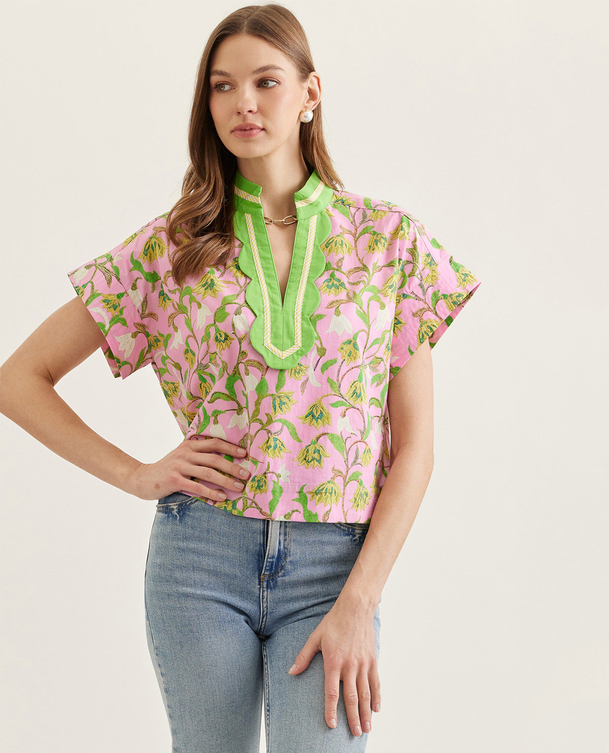 Woman wearing a pink floral blouse with green accents and blue jeans on a light background