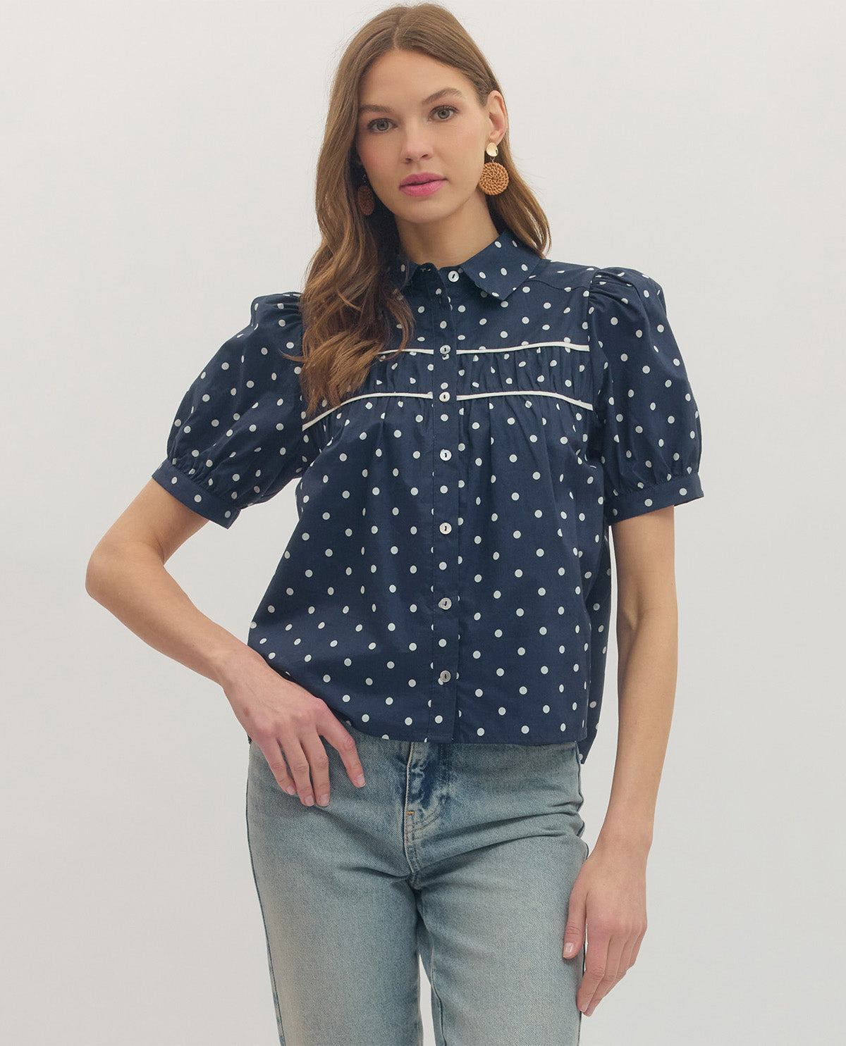 Woman wearing a navy blue polka dot blouse with short sleeves on a white background