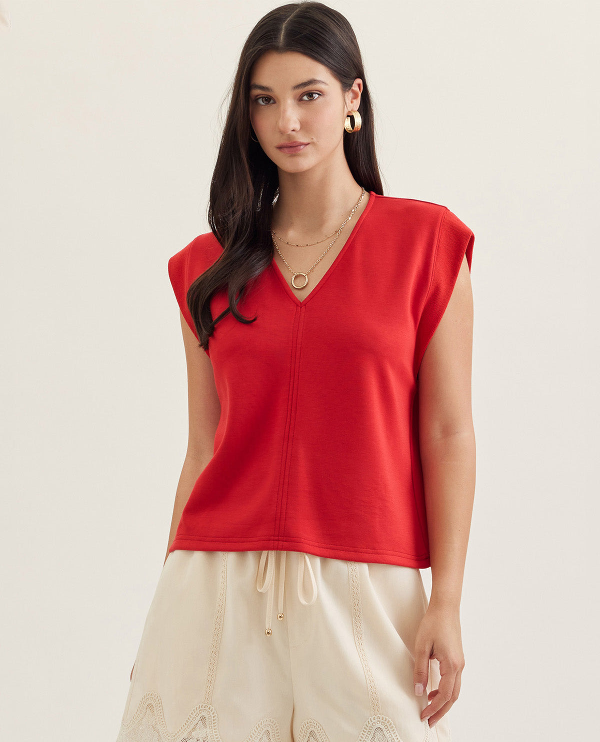 Woman wearing a red sleeveless top and beige pants on a light background
