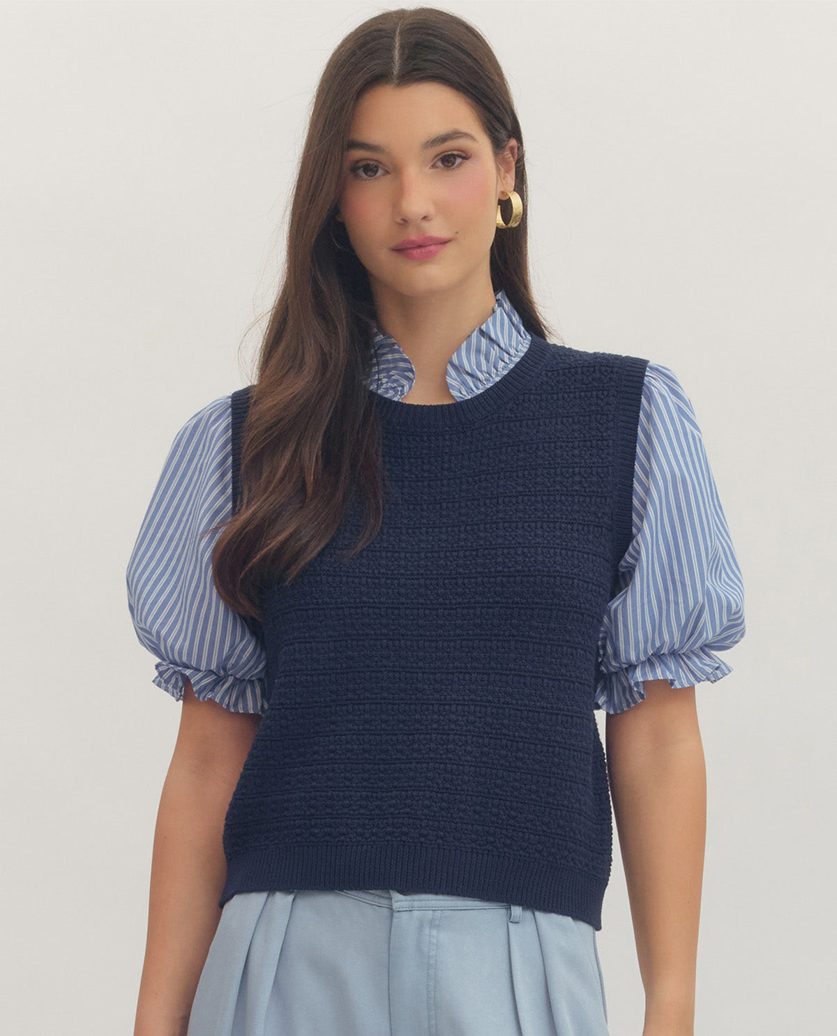 Woman wearing a navy knit vest over a striped shirt with a plain background