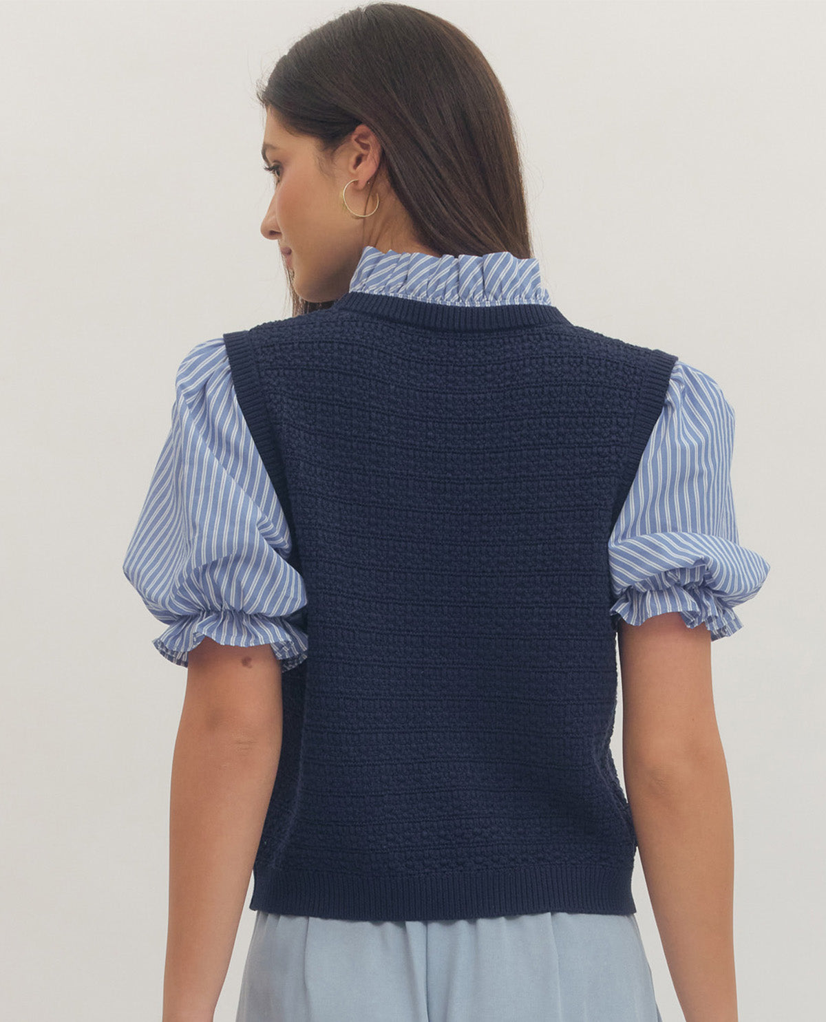 Woman wearing a navy knit vest over a blue and white striped shirt on a plain background