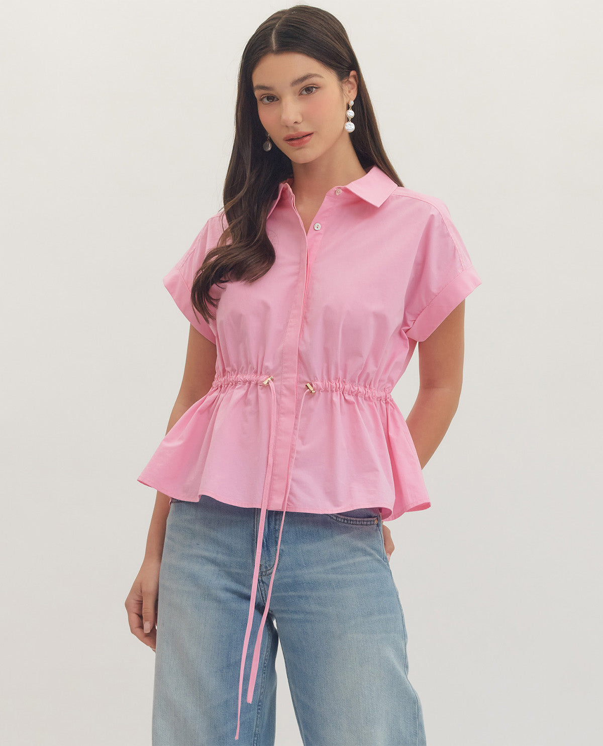Woman wearing a pink peplum top and blue jeans on a plain background