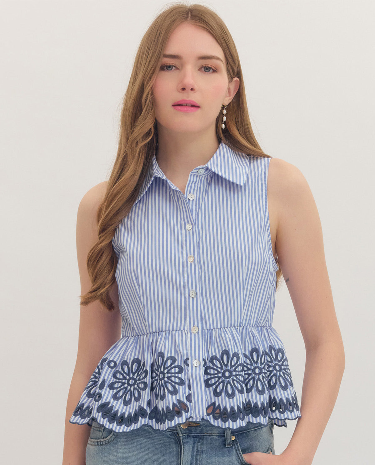Woman wearing a sleeveless blue and white striped top with floral embroidery on a plain background