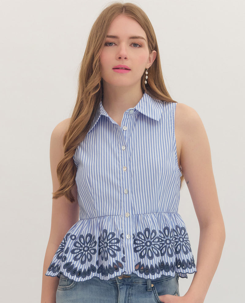 Woman wearing a sleeveless blue and white striped top with floral embroidery on a plain background
