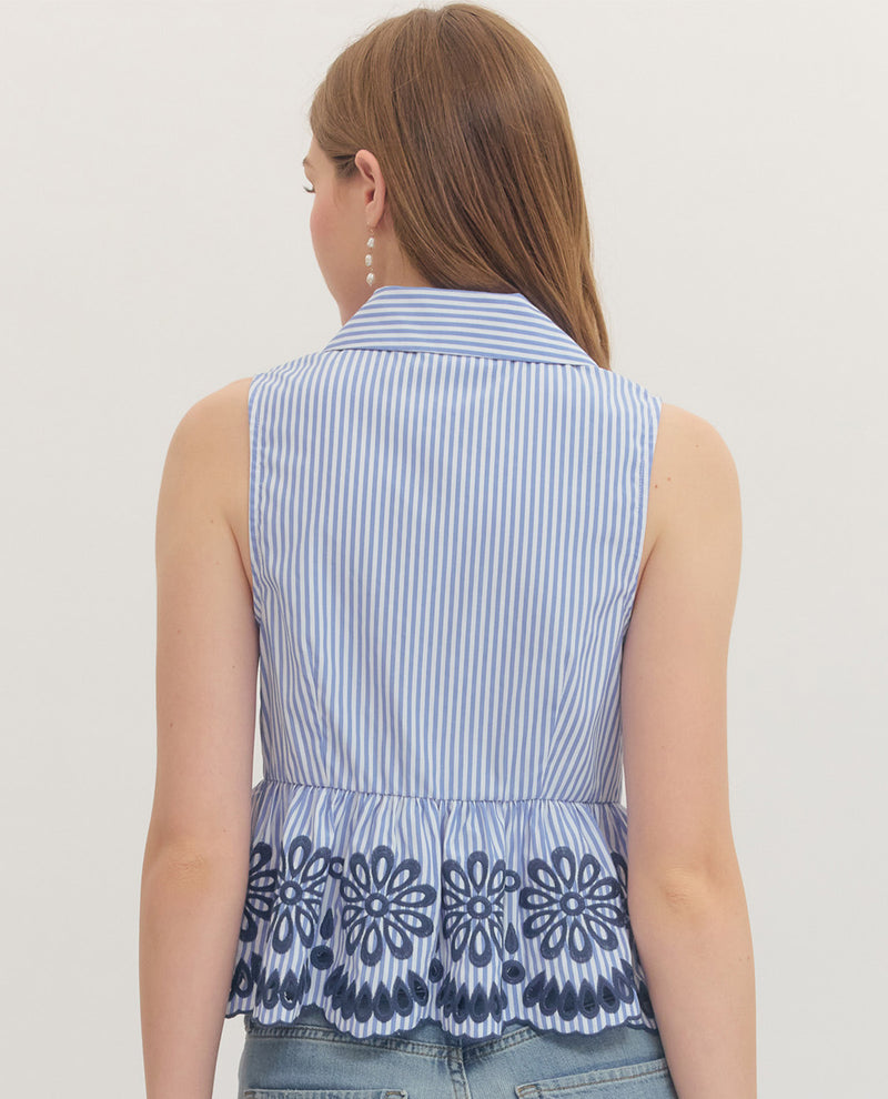 Woman wearing a sleeveless blue and white striped top with floral embroidery on a plain background
