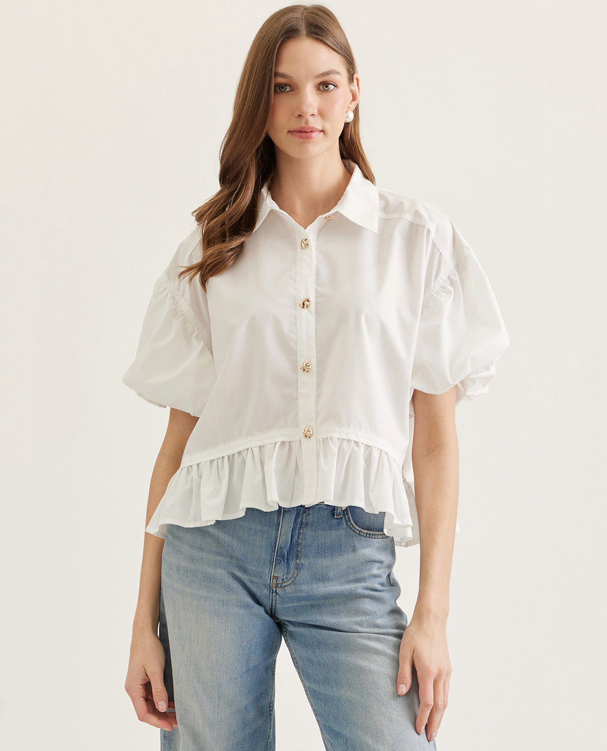 Woman wearing a white blouse with ruffled details and blue jeans on a light background