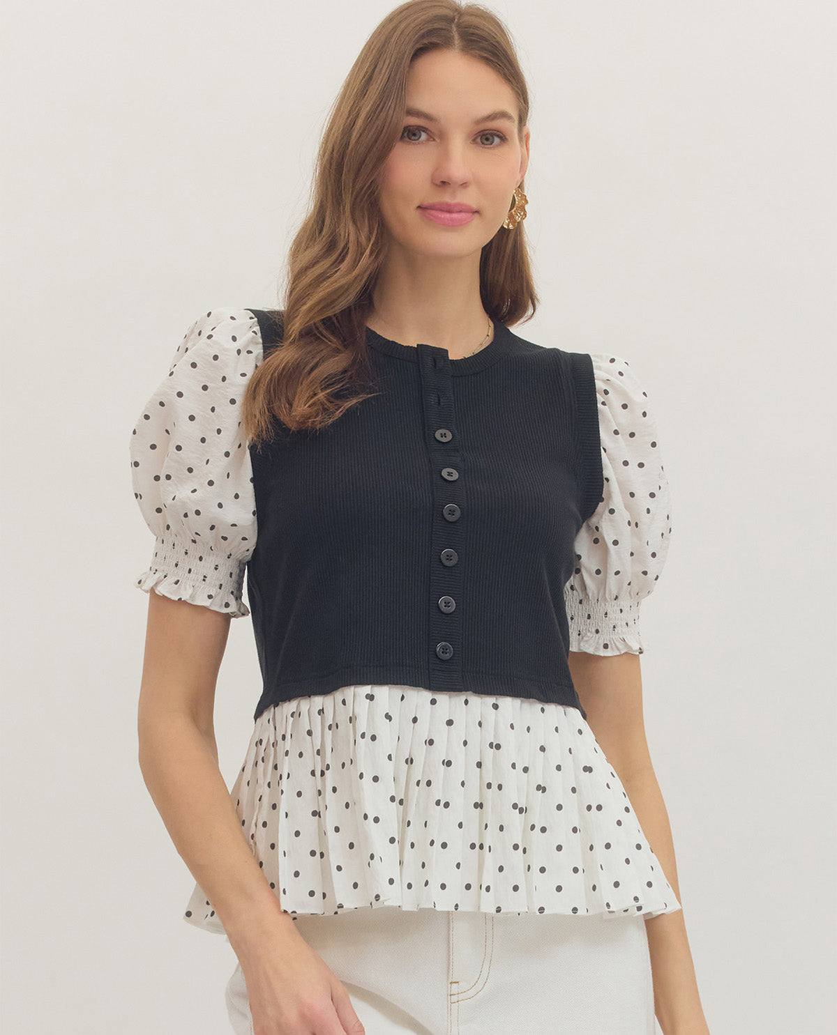 Woman wearing a black vest over a polka dot blouse with a white background