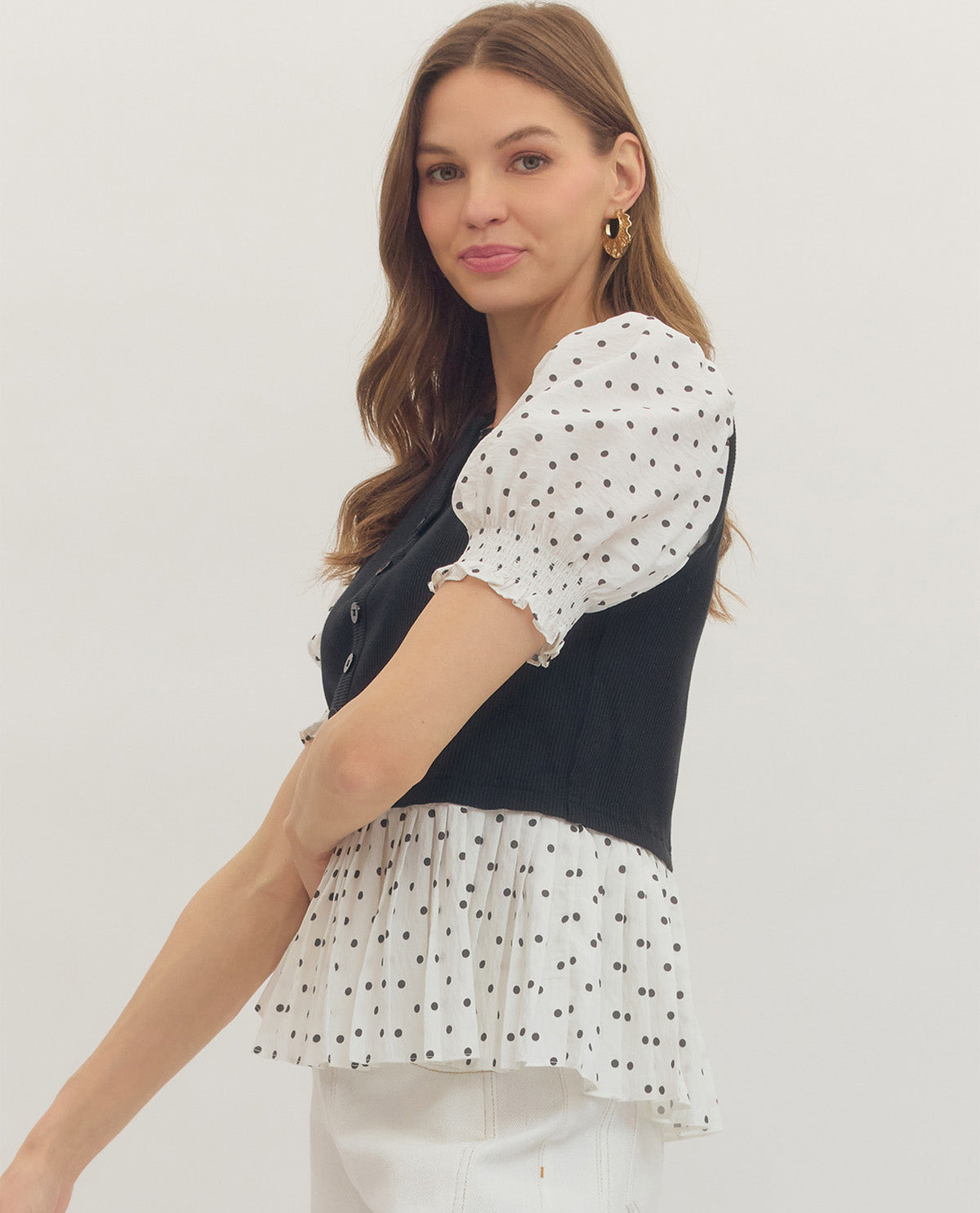 Woman wearing a black and white polka dot blouse with a plain background