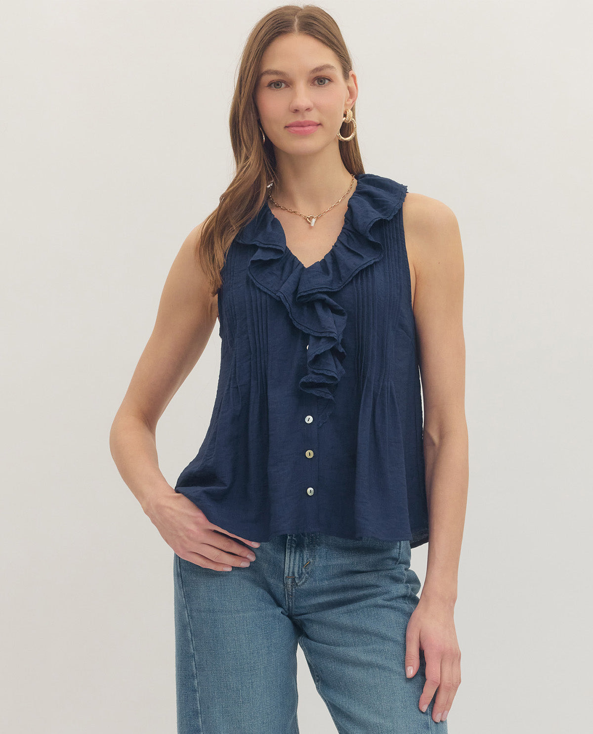 Woman wearing a navy blue sleeveless top with ruffles and jeans on a light background