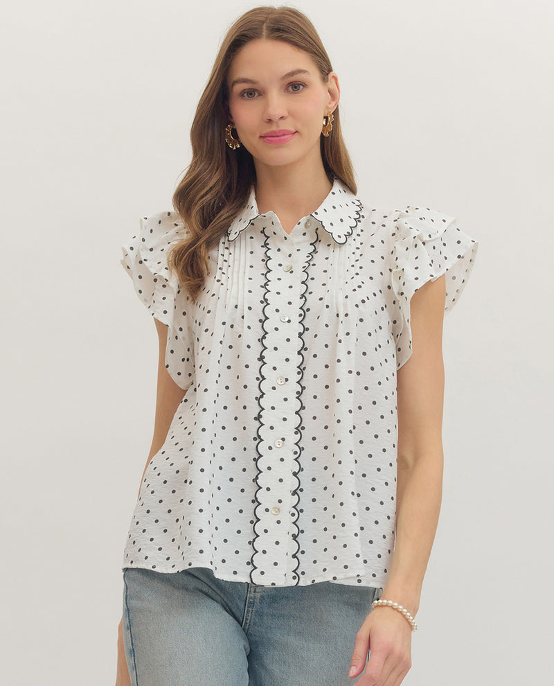 Woman wearing a white blouse with black patterns on a plain background