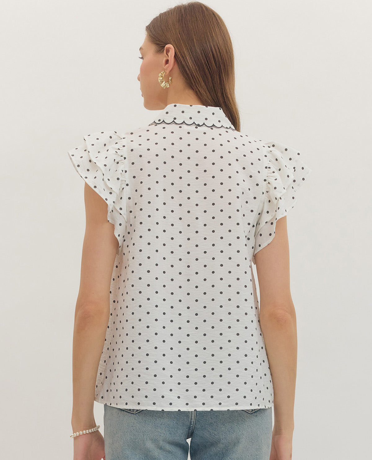 Woman wearing a white blouse with black polka dots and light blue jeans on a plain background