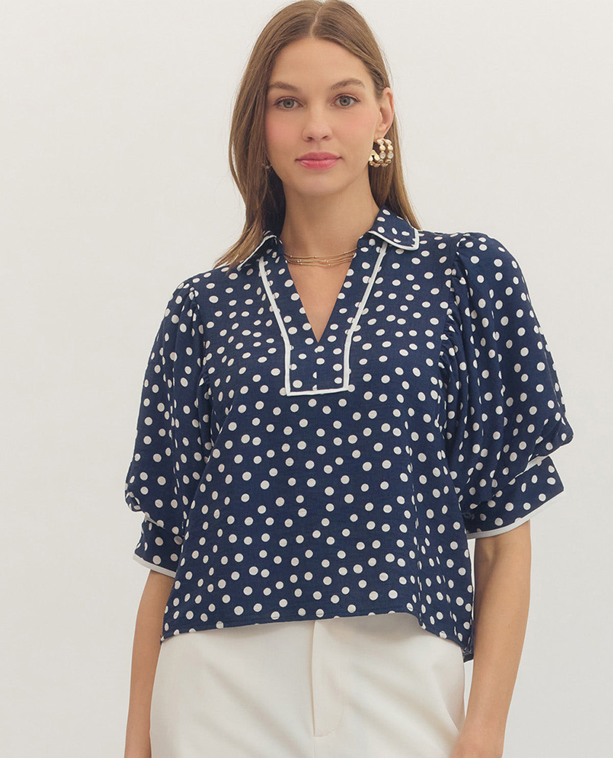 Woman wearing a navy blue blouse with white polka dots on a plain background