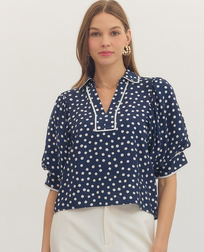 Woman wearing a navy blue blouse with white polka dots on a plain background