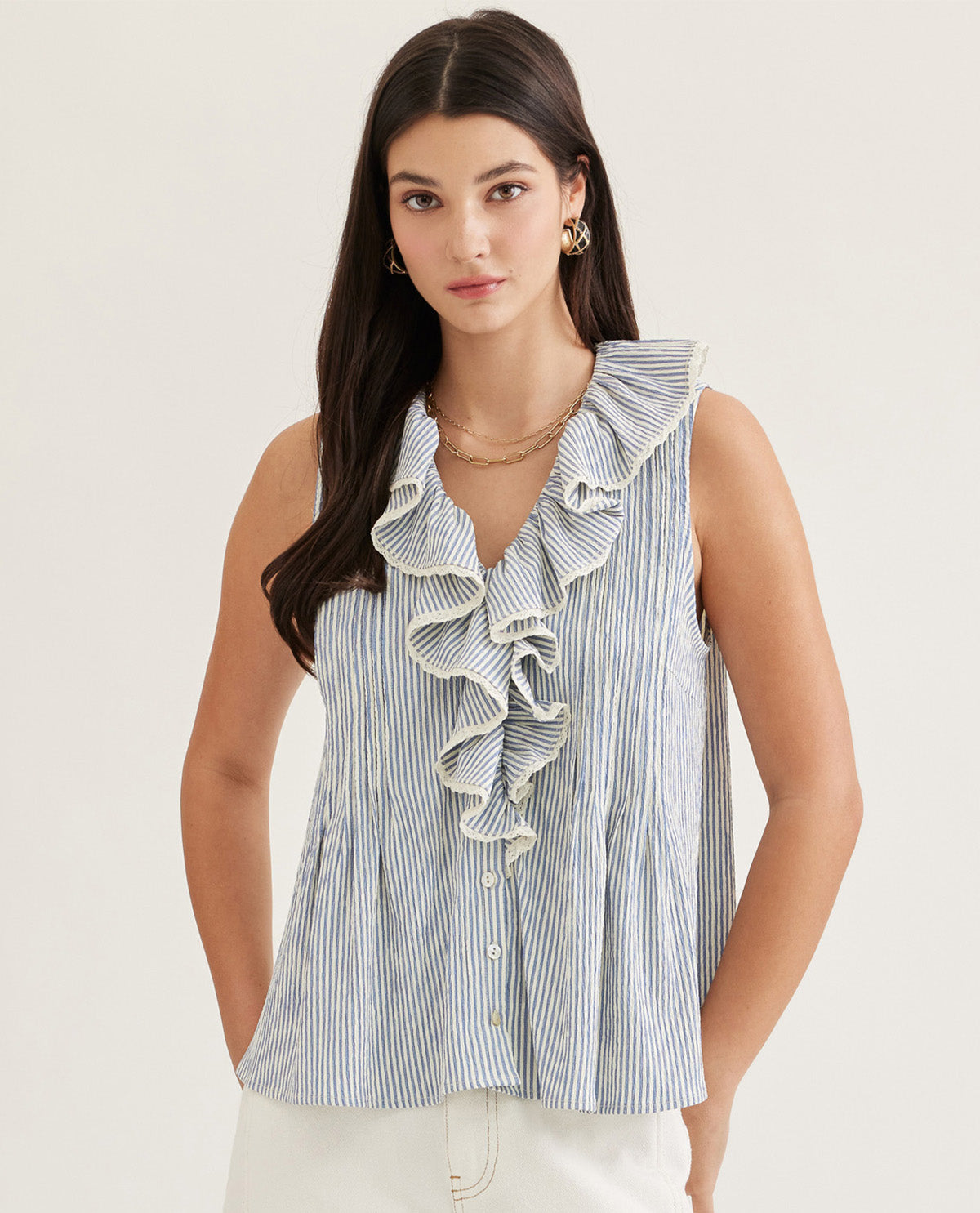 Woman wearing a blue and white striped sleeveless top with ruffles on a plain background
