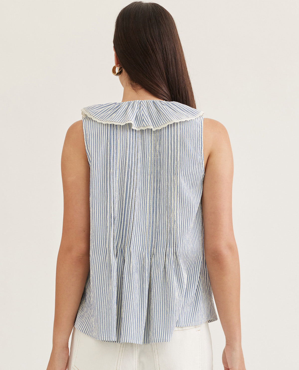 Woman wearing a sleeveless striped shirt with a ruffled collar on a plain background
