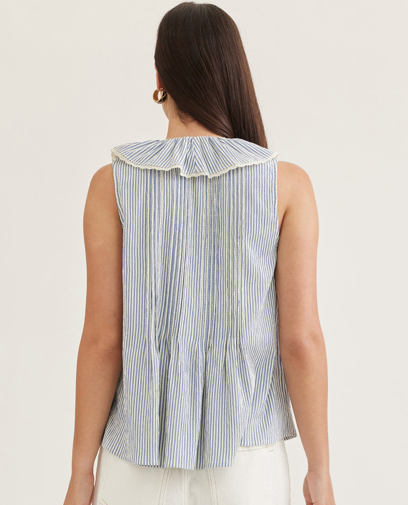 Woman wearing a sleeveless striped shirt with a ruffled collar on a plain background