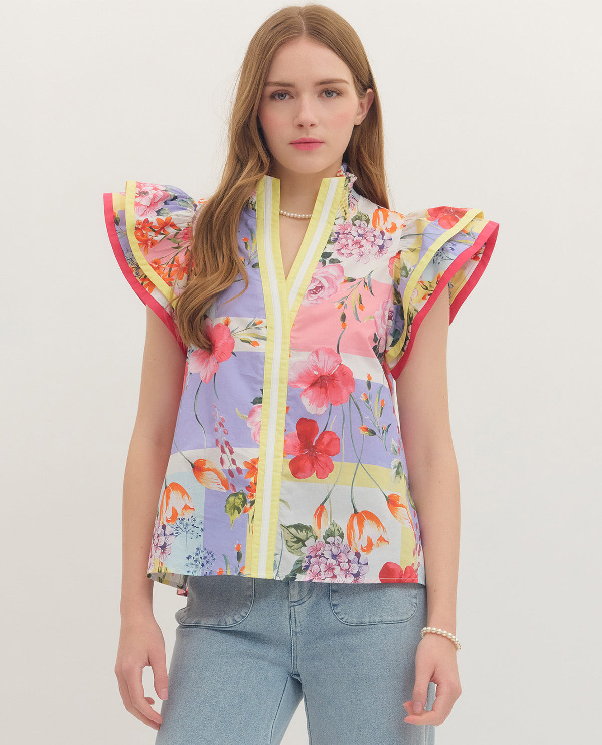 Woman wearing a colorful floral blouse with ruffled sleeves on a plain background