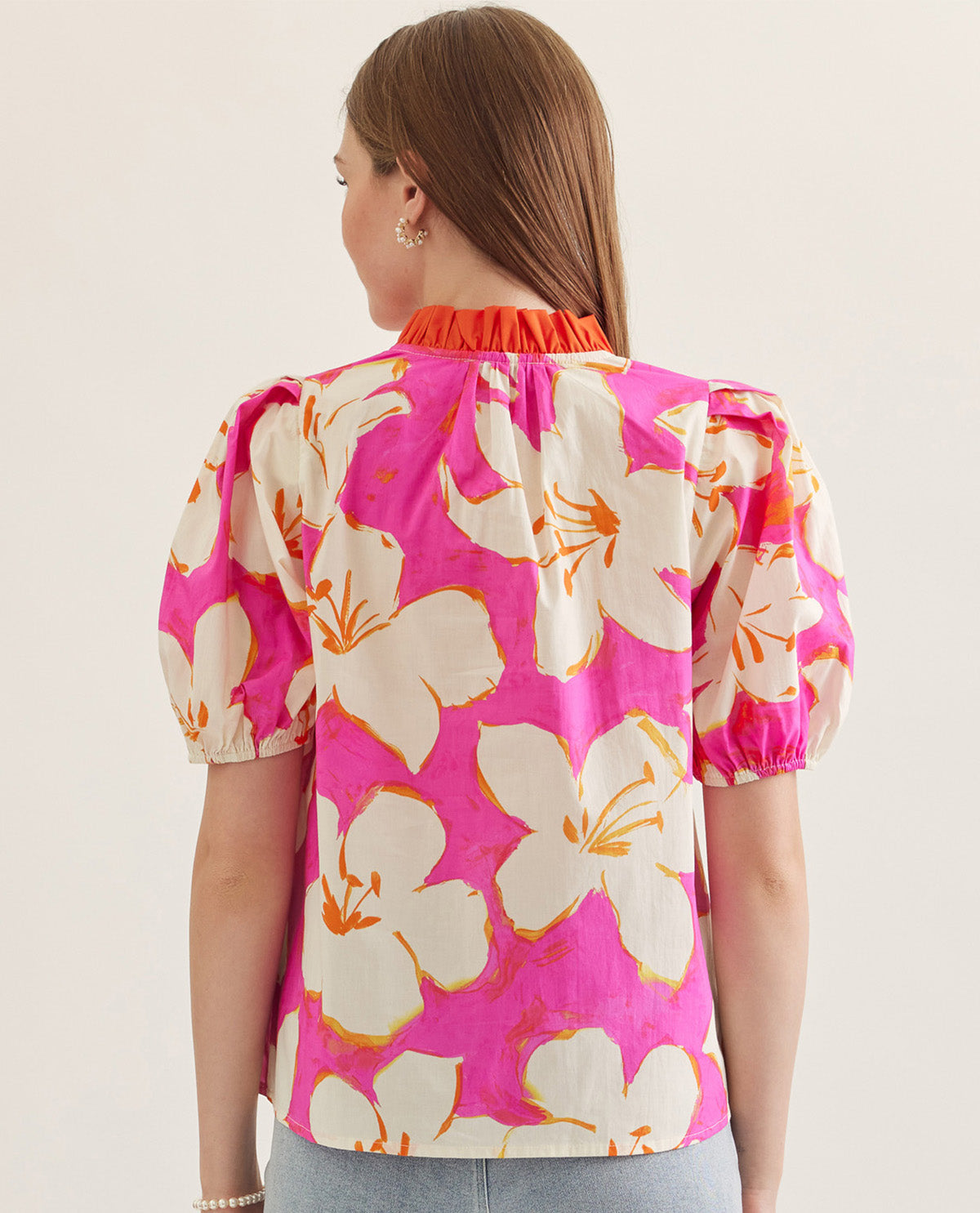 Woman wearing a pink floral blouse with puff sleeves on a plain background
