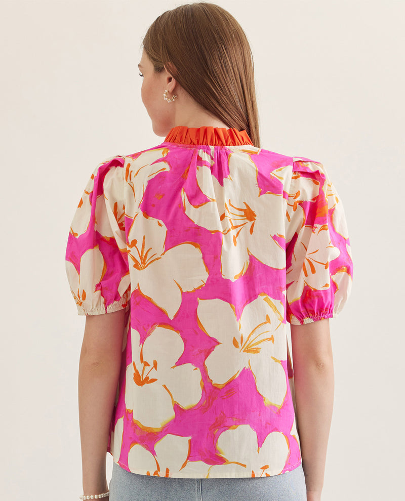 Woman wearing a pink floral blouse with puff sleeves on a plain background