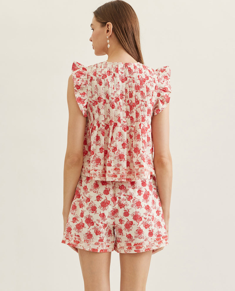 Woman wearing a red floral top and shorts on a plain background