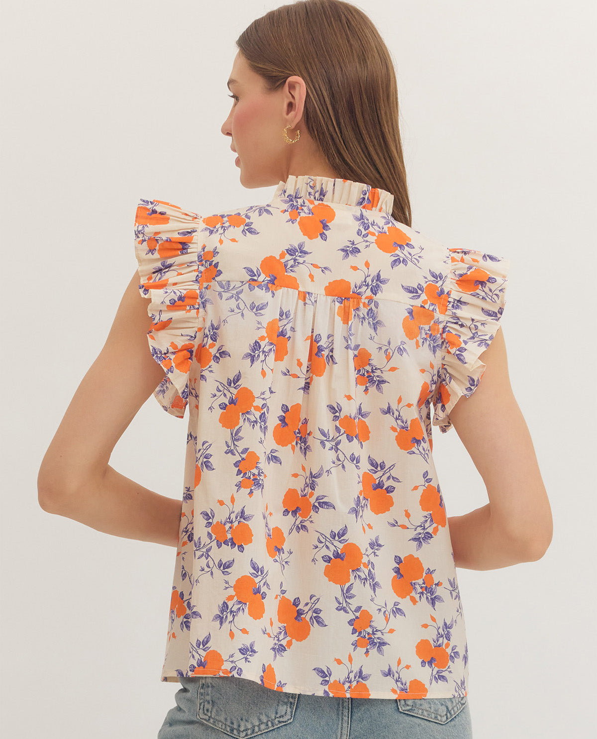 Woman wearing a floral blouse with orange and purple flowers on a plain background