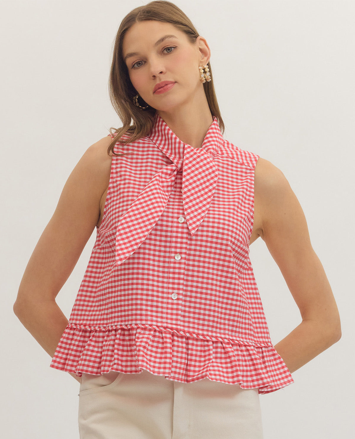 Woman wearing a red and white checkered blouse with a bow tie on a plain background