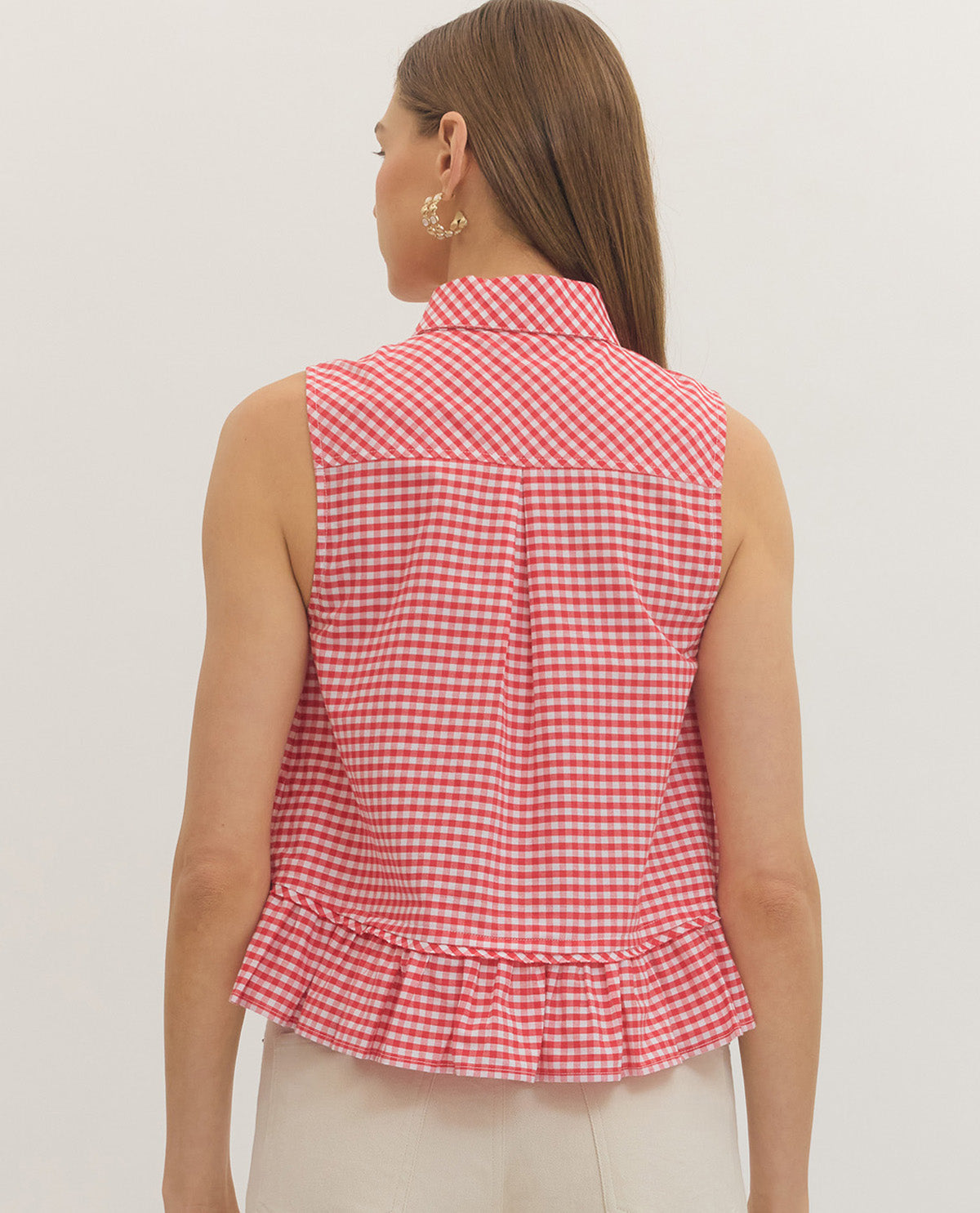 Woman wearing a red and white checkered sleeveless top on a plain background