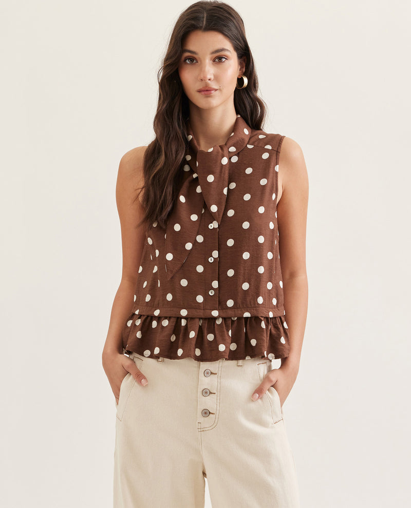 Woman wearing a brown polka dot sleeveless top with ruffled layers on a plain background