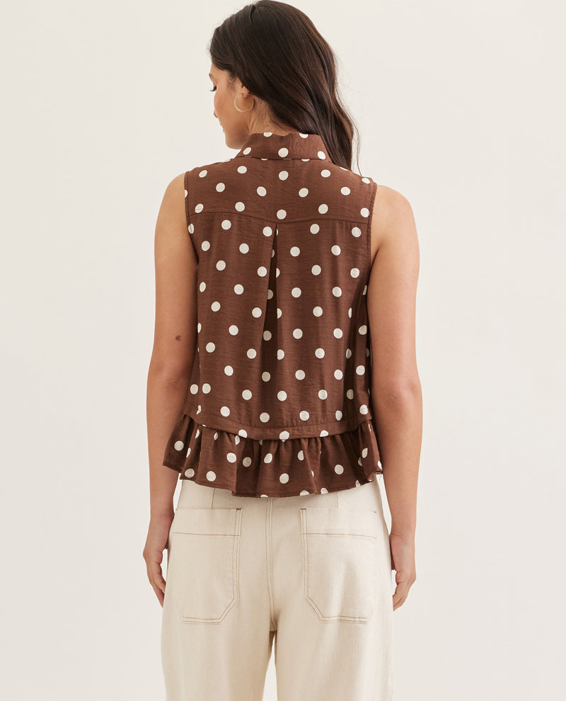 Woman wearing a brown polka dot sleeveless top with ruffled hem on a white background